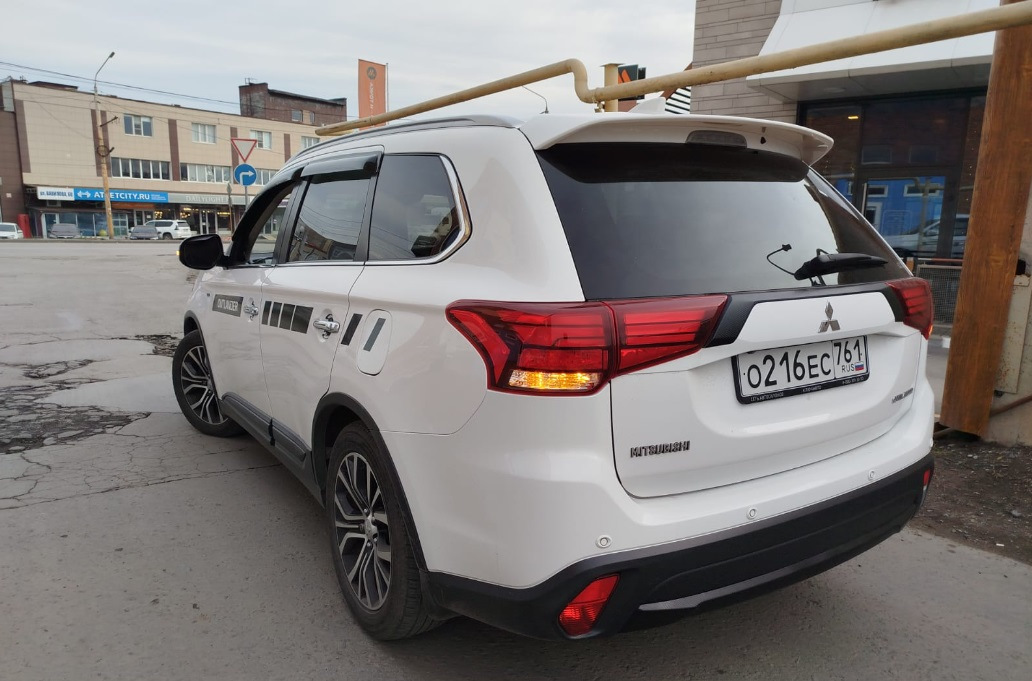 Спойлер — один из немногих элементов стайлинга для Outlander, который вызывает минимум споров — разумеется, с ним лучше, чем без него :)


Со спойлером теперь
Итак, заказал на Али сразу крашеный… По прикидкам некрашеный+покраска (зато точно в цвет) получалась примерно в 15Круб. Окрашеный сразу в белый — 4,3Круб. Решил рискнуть.

Пришел спойлер в транспортную компанию упакованный в пузырчатую пленку основательно, как мумия :)
И, тем не менее — сурпрыз! Заметный залом на внешнем ребре :(


Ну как так?
Ну в той 10-сантиметровой толщины обертке вряд ли так могло получиться, скорее всего сразу таким положили.
В-общем, подал спор (изначально подумал, что оспоренный деньги отдам мастерам, чтобы шпатлевали и красили). Отспорил 1,8Круб. То есть спойлер с дефектом обошелся в 2,5Круб.


По цвету — очень хорошее попадание, разве что на спойлере есть примесь блестящая (наверное, это Polar White или как его там). Но с завода бампера от кузова отличаются существенно сильнее :)
Уже начал у знакомых спрашивать, кто занимается такими работами, никто не признавался… повертел-покрутил в руках и решил кое-что попробовать :)

Сделал технологическое отверстие на внутренней стороне, обмотал изолентой наконечник длинной отвертки, нагрел спойлер в теплой воде, арендовал у жены фен и поставил его на минимальный нагрев.
Ну и изнутри минут за 30 осторожненько выровнял дефект.


Технологическое отверстие и инструмент
Пару недель спойлер отлежался на балконе (проверил, не сработает ли эффект памяти у пластика, когда остынет). Дефект проявился прям минимально (и то, это я знал, куда смотреть). Еще минут 10 повторил процедуру поддавливания и нагрева — и вуаля! Результат отличный.


Живьем вообще место дефекта не найдешь
Следующим квестом оказалось прикрепление.
Дальнейший текст скорее всего будет более интересен ростовчанам…

Беглый поиск стекольного герметика и праймера показал, что это добро обойдется в пару тысяч, не меньше. И потом почти весь герметик все равно на выброс…
Заехал в пару мест, где устанавливают стекла. В одном (федеральная сетка, АвтоТрейд) сразу сказали, что у них нет такой услуги в прайсе, а "внепрайсовые работы" караются штрафом и вплоть до увольнения. Но общались вежливо.

В другом (с довольно живыми социальными сетями, вроде как позиционирующие себя положительно, Автостекла на Вавилова) — просто вышел чувак, ни здрасте, ни досвидания, просто сказал "нет, я это делать не буду" и развернулся. Резкий контраст с социальными сетями. Неприятный осадочек :)

Уже подумал — ну всё, придется самому материалы покупать и звать кого-нибудь на помощь для ровной установки. Но решил заглянуть к еще одним установщикам автостекол. Оказалось, неподалеку есть AG Experts. Ребята красавчики — и пообщались вежливо, и один парень вышел посмотрел-пощупал спойлер. Согласились сделать. Подошли прям очень профессионально — все обезжирили, нанесли праймер, погрели феном и спойлер и крышку багажника, нанесли герметик, приклеили спойлер. И стоимость услуги нормальная — 1,5Круб.


Кепка
В-общем, теперь Белый Бумбр со спойлером.
Считаю, что он делает внешний вид аута существенно гармоничнее. Плюс стоимость доработки получилась ну очень приятной.